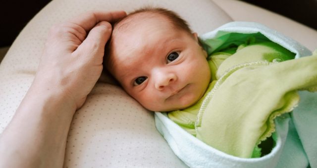 niemowlę patrzące w obiektyw głaskane po głowie