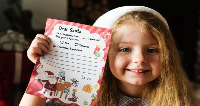 dziewczynka uśmiechająca się do obiektywu pokazująca swój list do świętego mikołaja