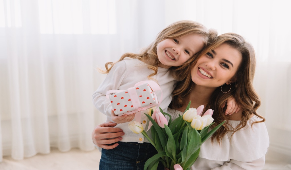 mama i córka w uścisku mama trzyma w rękach kwiaty córka wręcza jej prezent