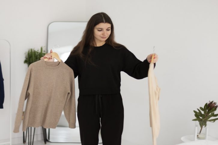 kobieta stojąca w mieszkaniu w obu dłoniach trzymająca wieszaki z ubraniami