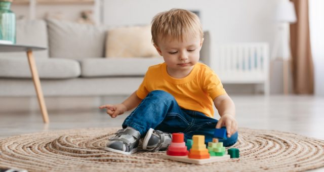 3-latek chłopiec bawiący się na dywanie w pokoju, układając wieże z klocków