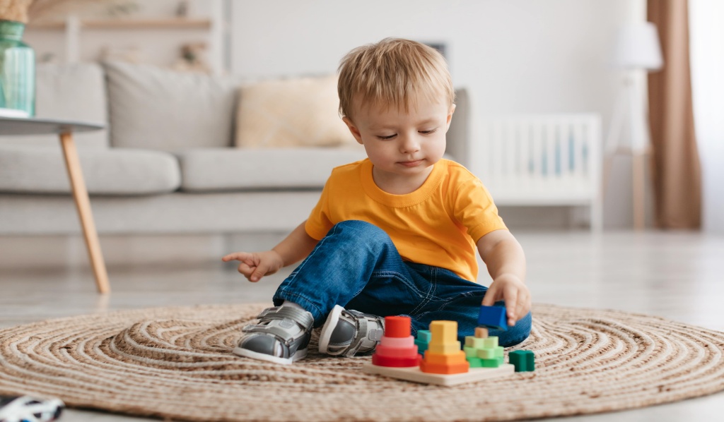 3-latek chłopiec bawiący się na dywanie w pokoju, układając wieże z klocków