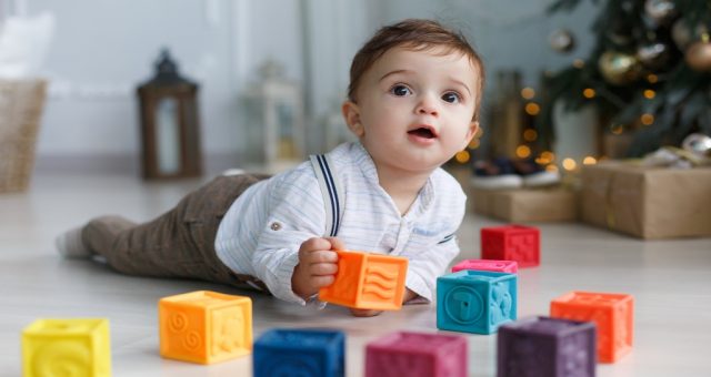 Dziecko leżące na brzuchu na dywanie, bawiące się klockami